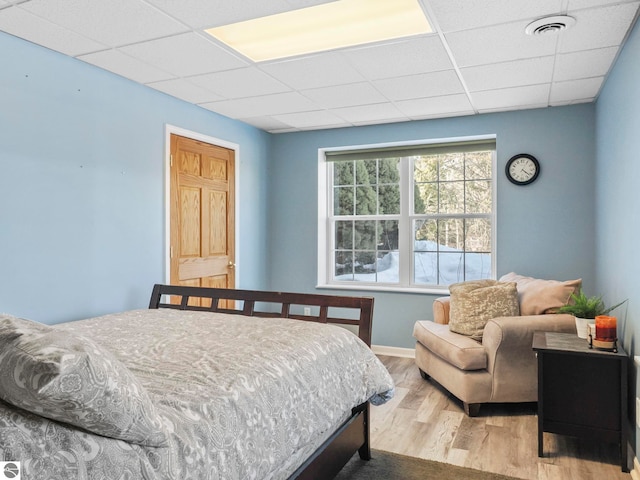 bedroom with a paneled ceiling, visible vents, baseboards, and wood finished floors