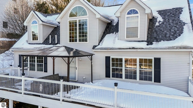 snow covered back of property featuring a shingled roof, a deck, and a gazebo