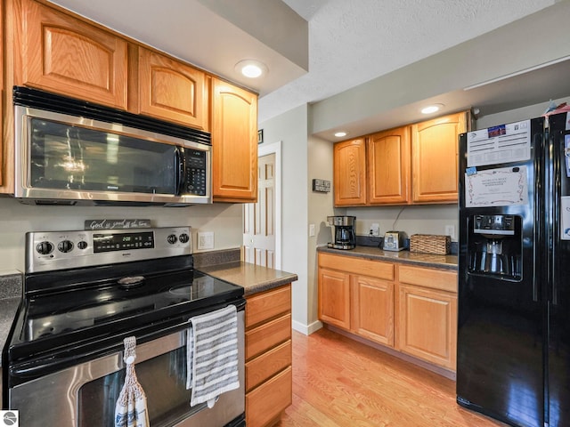 kitchen with stainless steel appliances, dark countertops, light wood-style flooring, and a textured ceiling