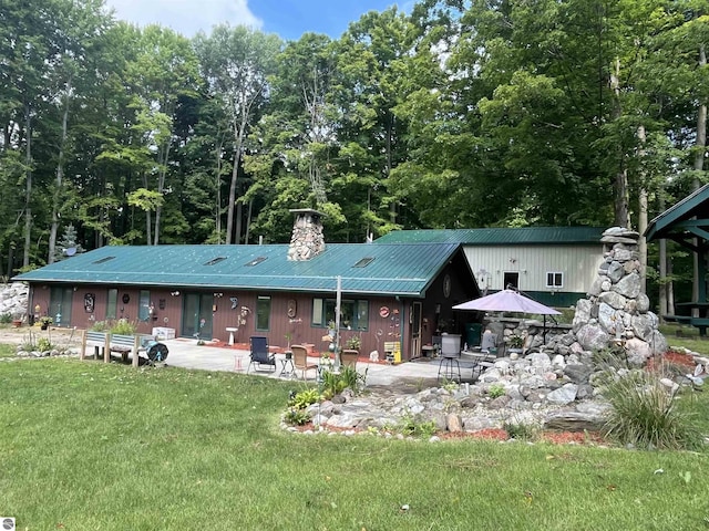 view of front facade with metal roof, a chimney, a front lawn, and a patio