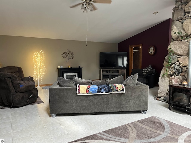 living room with a wood stove, light tile patterned flooring, vaulted ceiling, and ceiling fan