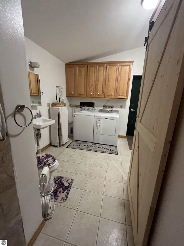 laundry area featuring light tile patterned floors, a barn door, separate washer and dryer, a sink, and cabinet space