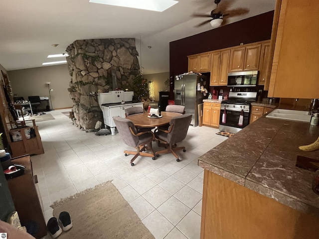 kitchen featuring light tile patterned floors, lofted ceiling with skylight, ceiling fan, stainless steel appliances, and a sink