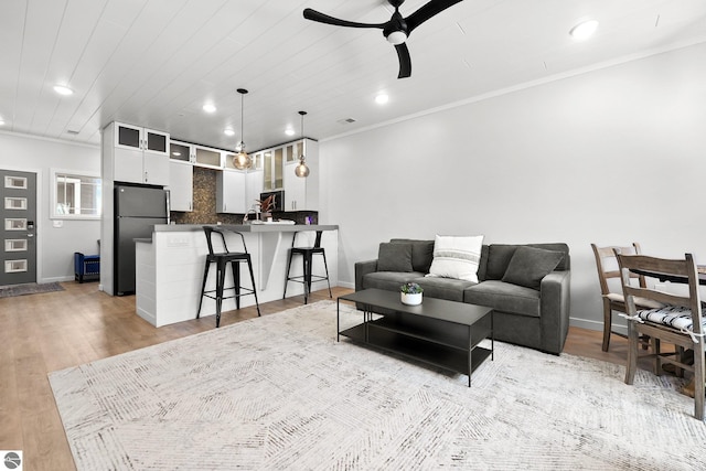 living room with crown molding, ceiling fan, light wood-style flooring, and baseboards