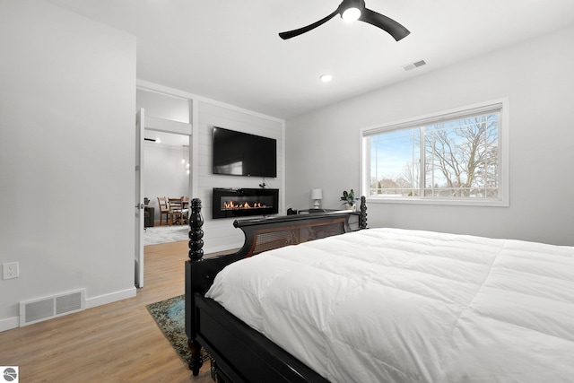 bedroom featuring a large fireplace, light wood-type flooring, visible vents, and baseboards