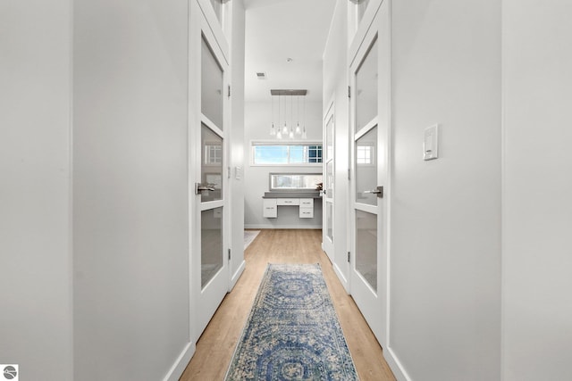 hallway with light wood-type flooring, baseboards, and french doors