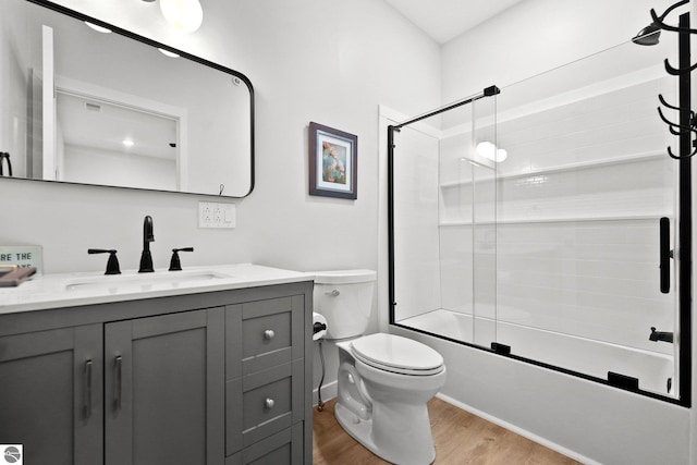 bathroom featuring toilet, bath / shower combo with glass door, wood finished floors, and vanity