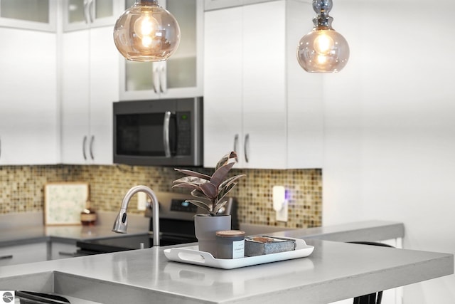 kitchen with tasteful backsplash, stainless steel microwave, white cabinets, and pendant lighting