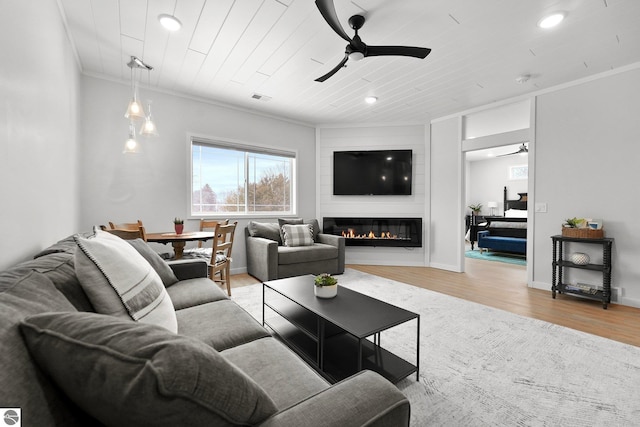 living room featuring visible vents, light wood-style flooring, ceiling fan, crown molding, and a fireplace