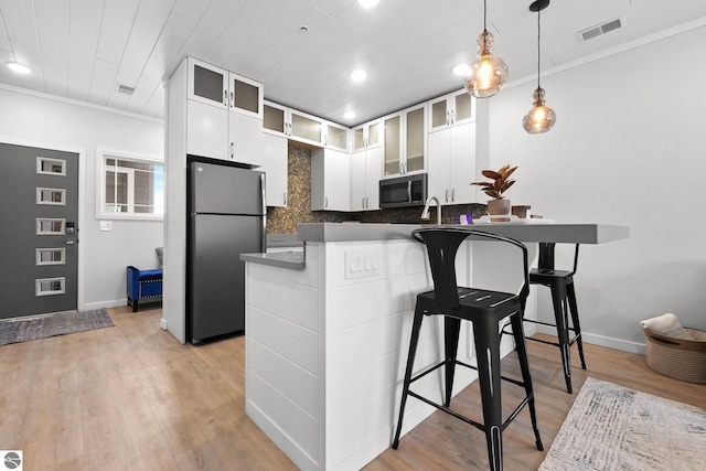 kitchen featuring visible vents, stainless steel microwave, a kitchen breakfast bar, freestanding refrigerator, and light wood-type flooring