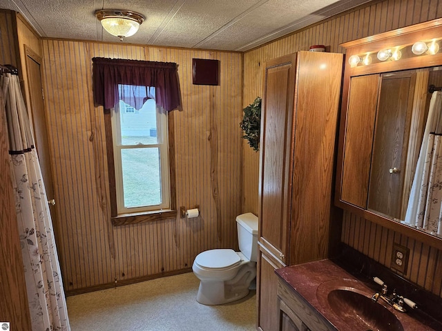 full bathroom featuring wooden walls, baseboards, toilet, a textured ceiling, and vanity