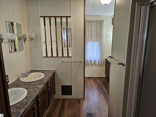 full bath with double vanity, wood finished floors, a sink, and visible vents