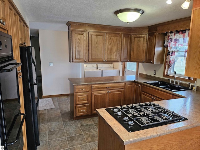 kitchen featuring a sink, a textured ceiling, independent washer and dryer, a peninsula, and black appliances