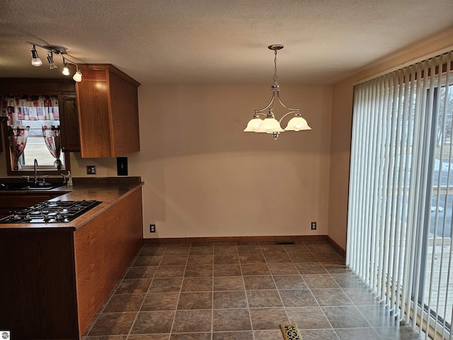 kitchen with baseboards, a sink, a textured ceiling, a notable chandelier, and black gas stovetop