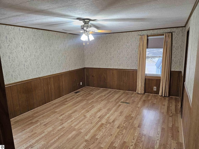 unfurnished room featuring wood finished floors, a wainscoted wall, a textured ceiling, and wallpapered walls