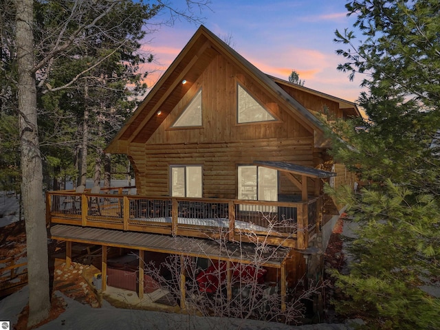 back of house at dusk with log exterior and a wooden deck