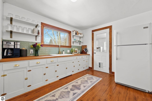 kitchen featuring open shelves, freestanding refrigerator, white cabinets, a sink, and wood finished floors