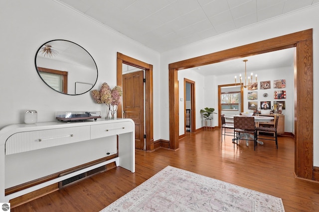 hall featuring ornamental molding, a notable chandelier, baseboards, and wood finished floors