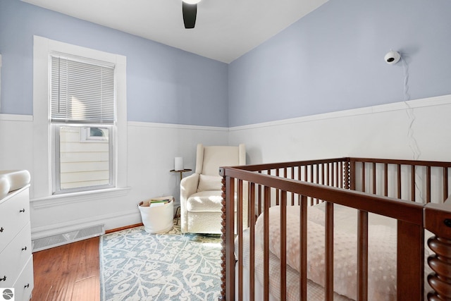 bedroom with a nursery area, wood finished floors, visible vents, and a ceiling fan