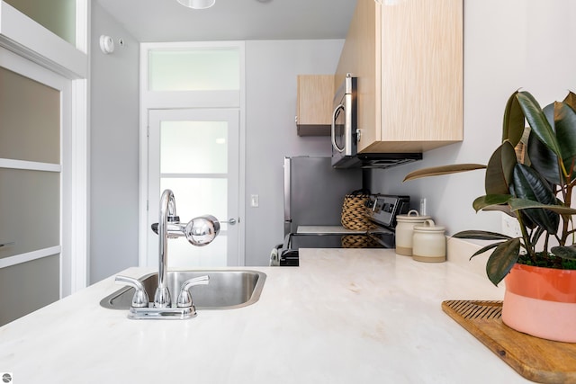 kitchen with stainless steel appliances, light countertops, light brown cabinets, a sink, and modern cabinets