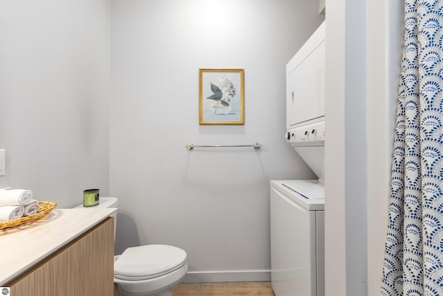 full bath featuring stacked washer and dryer, baseboards, toilet, wood finished floors, and curtained shower