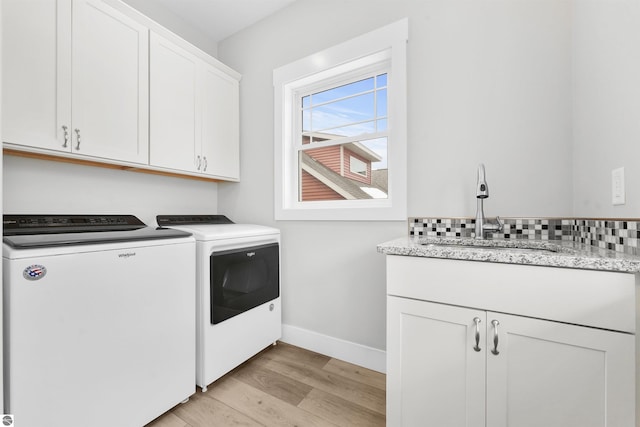 laundry area featuring washer and clothes dryer, cabinet space, light wood-style flooring, a sink, and baseboards