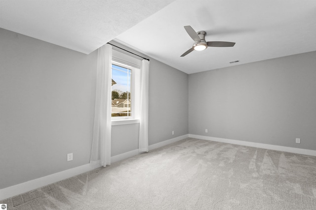 carpeted spare room featuring a ceiling fan, visible vents, and baseboards