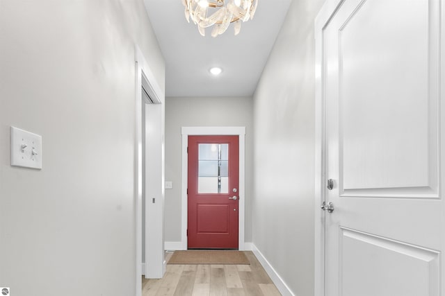 doorway to outside featuring light wood-style floors, baseboards, and an inviting chandelier