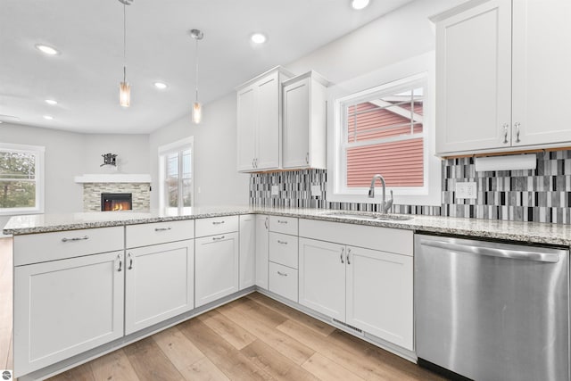 kitchen with a peninsula, a sink, light wood-style floors, a wealth of natural light, and dishwasher