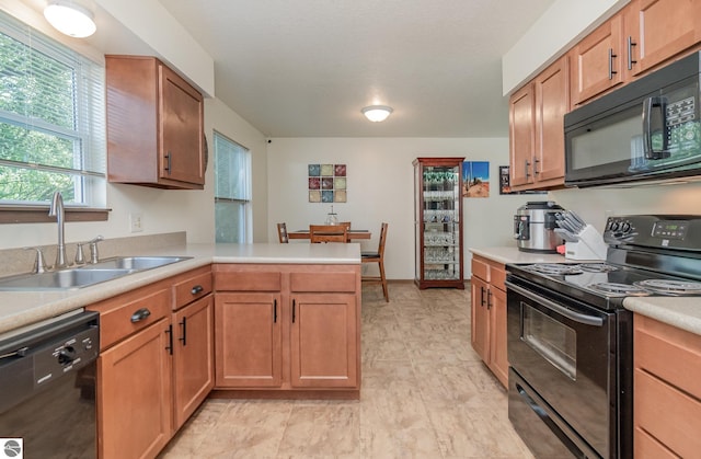 kitchen featuring brown cabinetry, a peninsula, light countertops, black appliances, and a sink