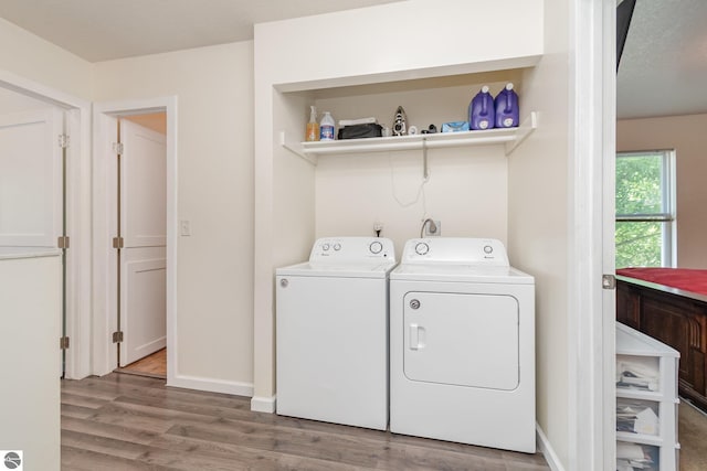 clothes washing area with laundry area, washer and clothes dryer, wood finished floors, and baseboards