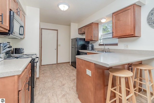 kitchen with a peninsula, a sink, light countertops, black appliances, and a kitchen bar