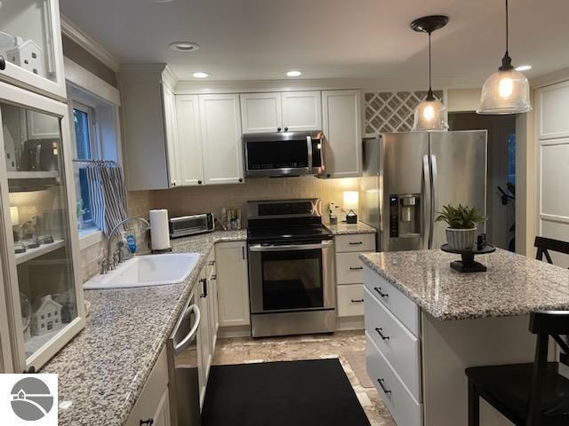 kitchen featuring backsplash, appliances with stainless steel finishes, a kitchen breakfast bar, white cabinets, and a sink