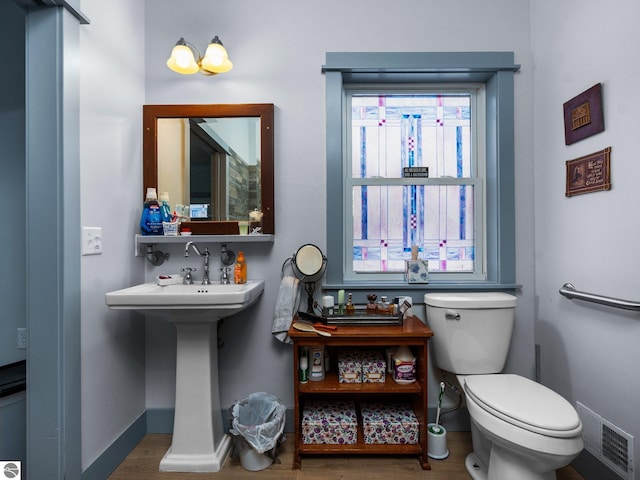 bathroom with visible vents, toilet, a sink, wood finished floors, and baseboards