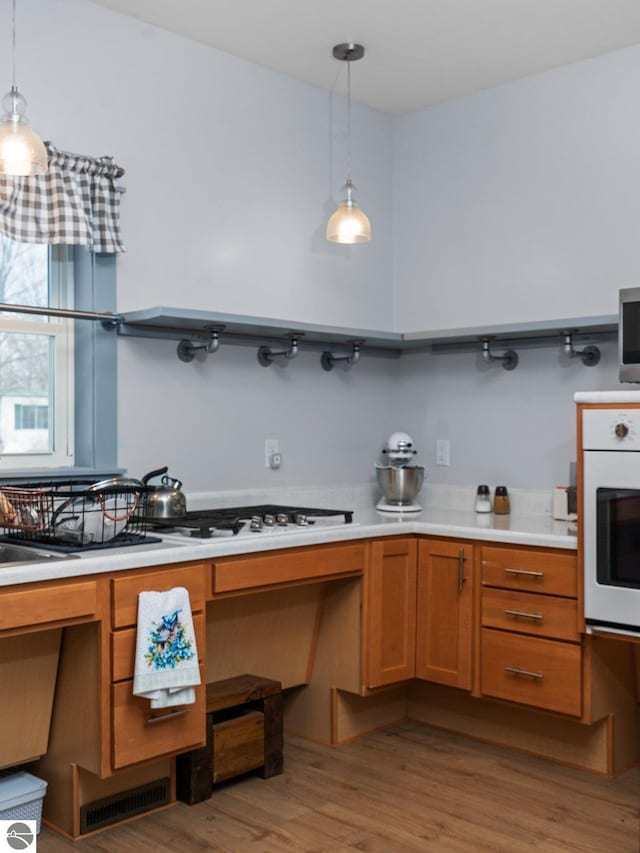 kitchen featuring brown cabinets, wood finished floors, decorative light fixtures, white oven, and light countertops