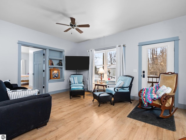 living area featuring a ceiling fan, baseboards, and light wood finished floors