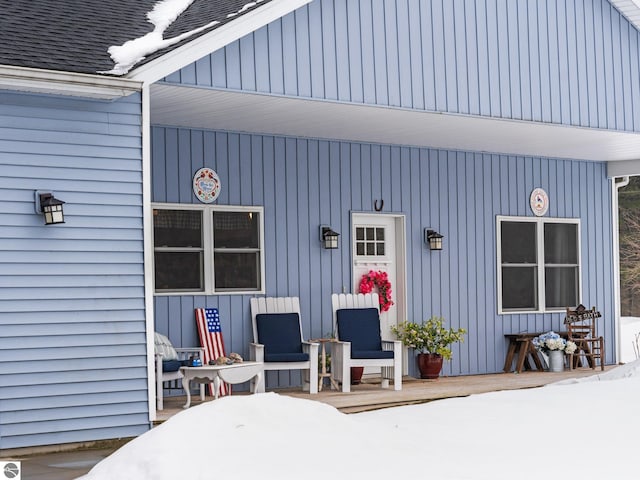 snow covered property entrance featuring a shingled roof and board and batten siding