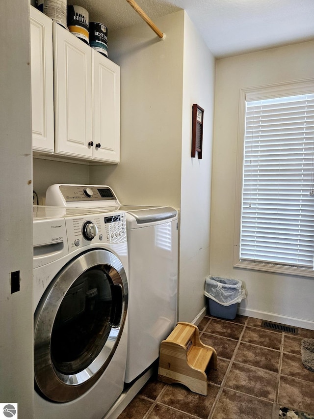 laundry room featuring dark tile patterned flooring, cabinet space, visible vents, washer and dryer, and baseboards