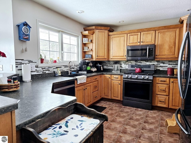 kitchen featuring stainless steel appliances, dark countertops, decorative backsplash, a sink, and dark tile patterned flooring