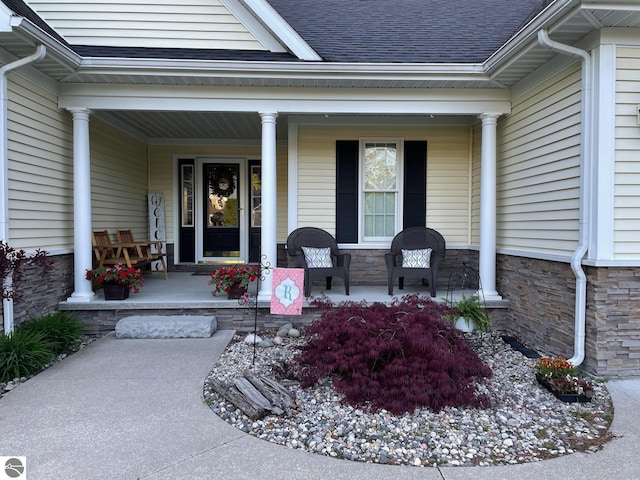 doorway to property featuring a porch, stone siding, and roof with shingles