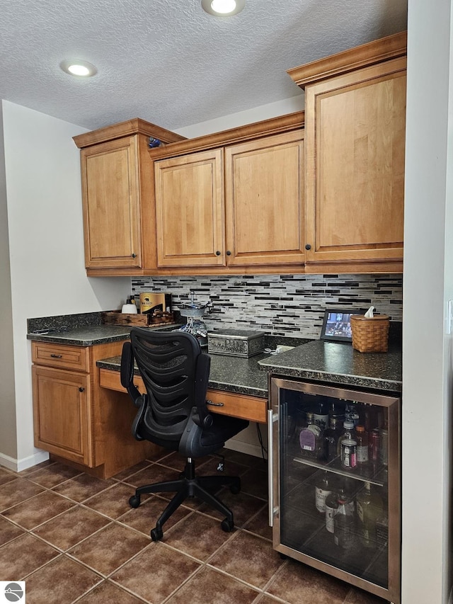 office with a textured ceiling, dark tile patterned flooring, wine cooler, and built in study area