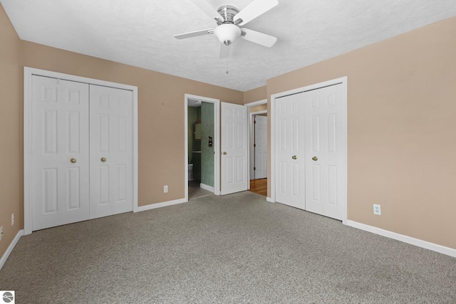 unfurnished bedroom featuring baseboards, ensuite bathroom, a textured ceiling, carpet floors, and two closets