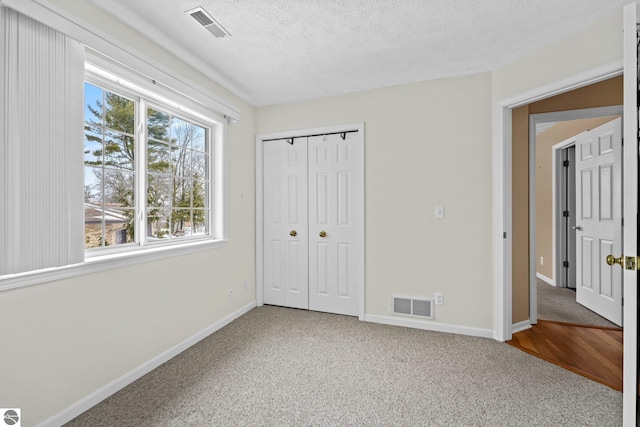 unfurnished bedroom featuring carpet floors, visible vents, a textured ceiling, and baseboards