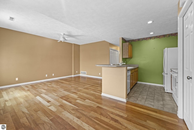 kitchen with a peninsula, light wood-style floors, visible vents, and brown cabinetry