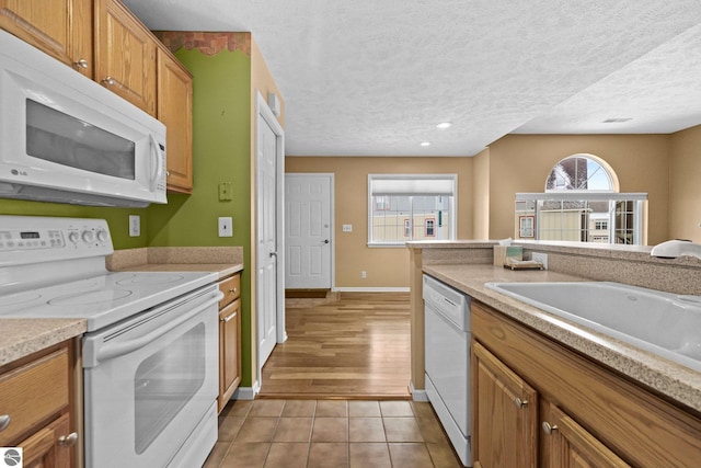 kitchen with a sink, white appliances, light tile patterned floors, and a textured ceiling