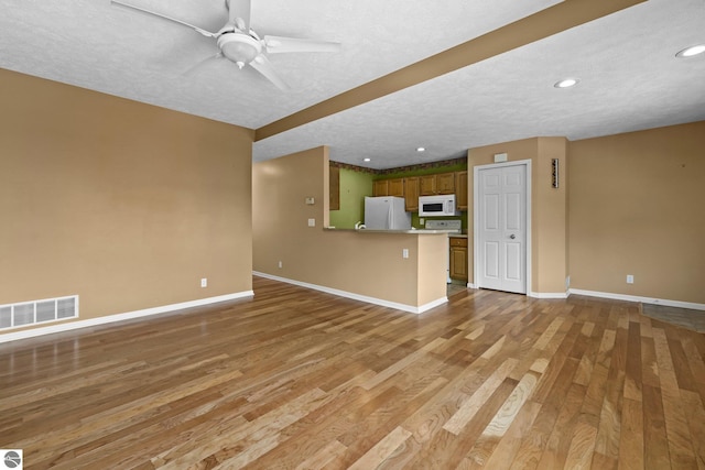 unfurnished living room featuring light wood-style floors, baseboards, visible vents, and a textured ceiling