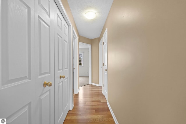 corridor featuring light wood-type flooring, a textured ceiling, and baseboards