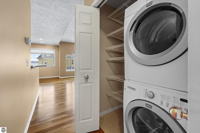 clothes washing area featuring stacked washer and dryer, a textured ceiling, wood finished floors, laundry area, and baseboards