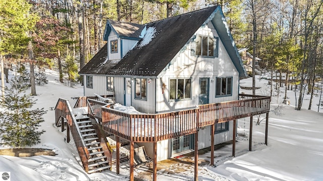 snow covered property featuring roof with shingles, stairway, and a wooden deck