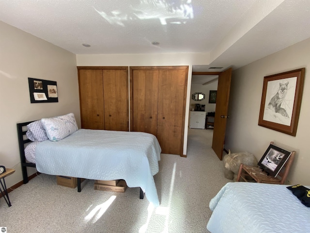 bedroom with light carpet, visible vents, a textured ceiling, and two closets